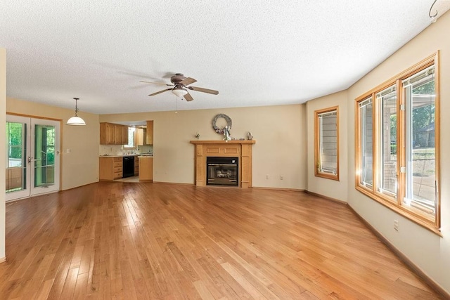 4 Wincanton Ln, Bella Vista, AR 72715 - unfurnished living room with light wood-style flooring, a textured ceiling, a ceiling fan, a glass covered fireplace, and baseboards