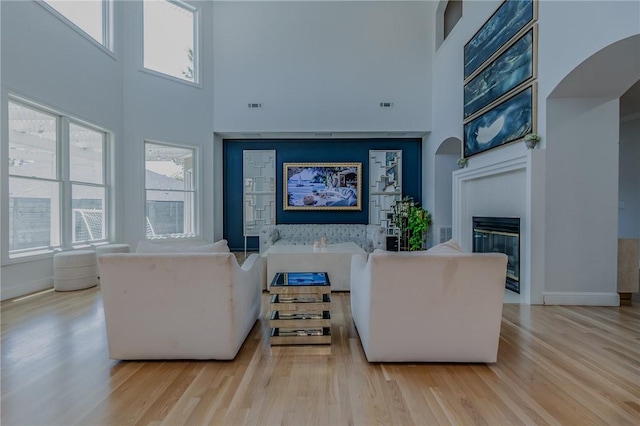 4 W Colonial Dr, Rogers, AR 72758 - living room featuring a high ceiling, light wood finished floors, a glass covered fireplace, plenty of natural light, and baseboards