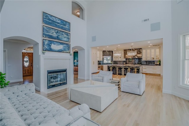 4 W Colonial Dr, Rogers, AR 72758 - living room featuring a high ceiling, arched walkways, light wood-type flooring, a glass covered fireplace, and healthy amount of natural light