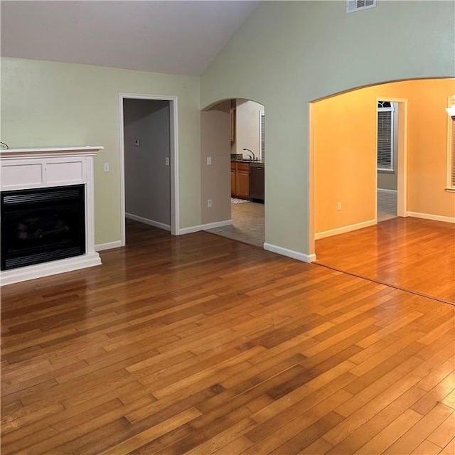 20944 Shady Grove Rd, Siloam Springs, AR 72761 - unfurnished living room with arched walkways, hardwood / wood-style flooring, a fireplace, high vaulted ceiling, and baseboards
