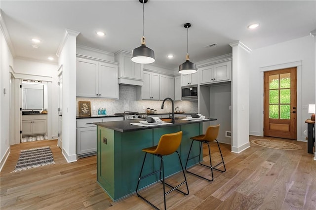 41 Westmorland Dr, Bella Vista, AR 72714 - kitchen featuring stainless steel microwave, dark countertops, light wood finished floors, backsplash, and a center island with sink