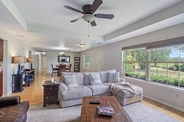 17171 Kincheloe Rd, Siloam Springs, AR 72761 - living room featuring a tray ceiling, light wood-type flooring, baseboards, a ceiling fan, and a chandelier