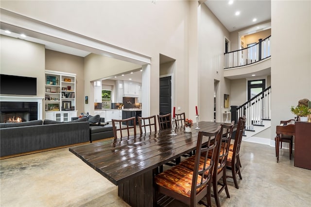 3634 Sugarberry Ln, Springdale, AR 72764 - dining room with finished concrete flooring, a warm lit fireplace, a towering ceiling, stairway, and baseboards