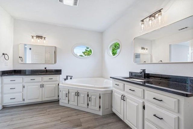 119 Elm St, Centerton, AR 72719 - bathroom featuring two vanities, a garden tub, and wood finished floors