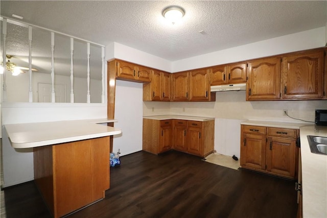 3064 Brandy Ln, Springdale, AR 72762 - kitchen featuring under cabinet range hood, brown cabinetry, dark wood-type flooring, a textured ceiling, and a peninsula