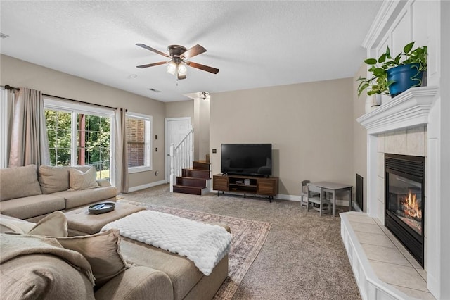 8200 Titleist Cir, Rogers, AR 72756 - carpeted living room featuring a tiled fireplace, stairway, a ceiling fan, baseboards, and a textured ceiling