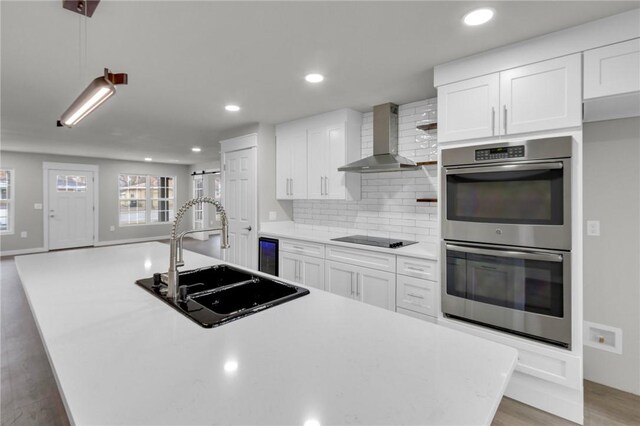 1115 Eicher Ave, Springdale, AR 72764 - kitchen with wall chimney exhaust hood, stainless steel double oven, a sink, a kitchen island with sink, and black electric cooktop