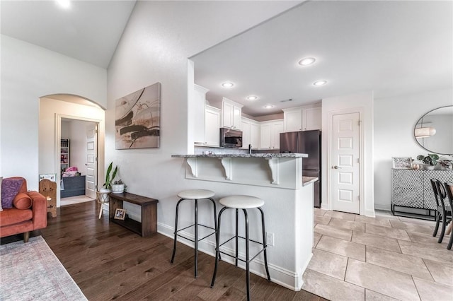 7533 Devonshire Ave, Springdale, AR 72762 - kitchen featuring stainless steel appliances, light stone counters, a breakfast bar area, arched walkways, and white cabinets
