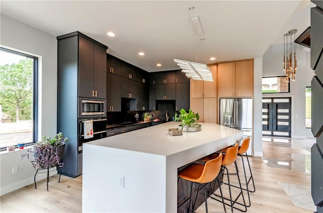 675 N Cliffside Dr, Fayetteville, AR 72701 - kitchen with appliances with stainless steel finishes, light wood-style floors, a kitchen bar, a kitchen island, and backsplash