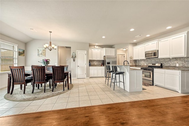811 SW Pure Globe St, Bentonville, AR 72712 - kitchen featuring appliances with stainless steel finishes, backsplash, a breakfast bar area, a chandelier, and light tile patterned floors