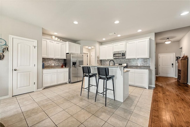 811 SW Pure Globe St, Bentonville, AR 72712 - kitchen with stainless steel appliances, tasteful backsplash, a kitchen breakfast bar, light tile patterned floors, and white cabinets