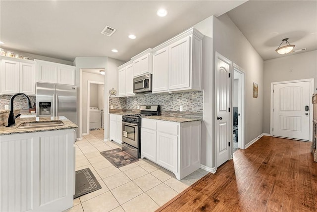811 SW Pure Globe St, Bentonville, AR 72712 - kitchen with appliances with stainless steel finishes, washer / dryer, a sink, decorative backsplash, and white cabinets