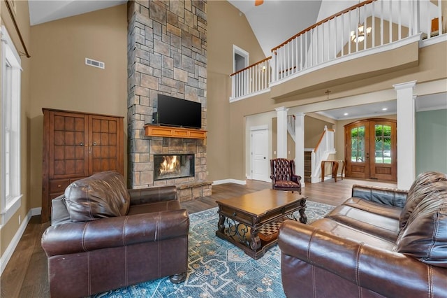 12292 Butler Rd, Prairie Grove, AR 72753 - living room featuring decorative columns, a stone fireplace, wood finished floors, high vaulted ceiling, and baseboards