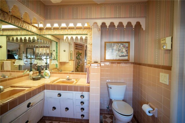 1617 Ranch Dr, Springdale, AR 72762 - bathroom with double vanity, toilet, tile walls, a wainscoted wall, and wallpapered walls
