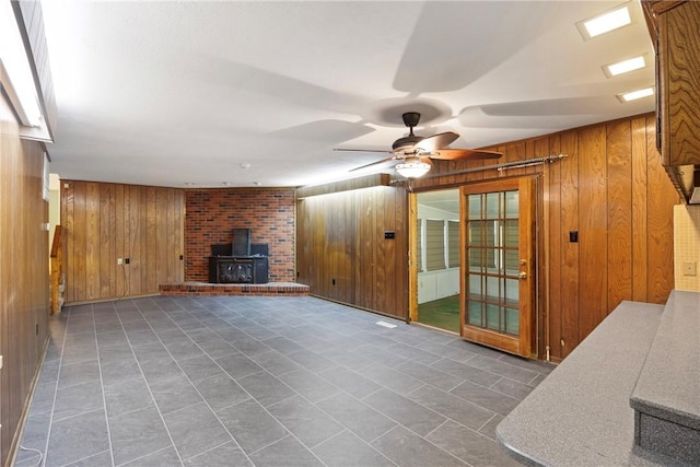 711 W 18th Ter, Russellville, AR 72801 - unfurnished living room with wooden walls, a wood stove, a ceiling fan, and tile patterned flooring