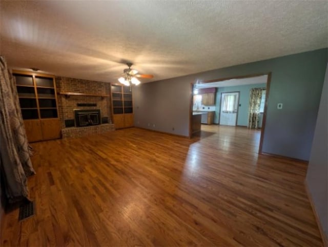 208 Mc 6087, Yellville, AR 72687 - unfurnished living room with ceiling fan, a textured ceiling, wood finished floors, and a brick fireplace