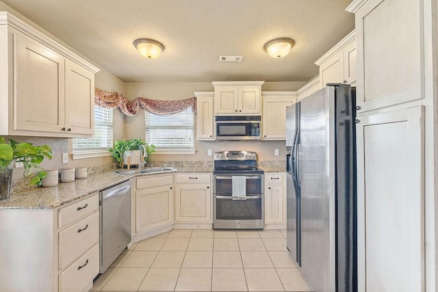 801 SW Castlewood St, Bentonville, AR 72712 - kitchen with appliances with stainless steel finishes, a sink, light tile patterned floors, a textured ceiling, and light stone countertops