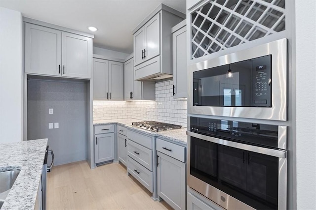 7101 SW Basswood Ave, Bentonville, AR 72713 - kitchen with appliances with stainless steel finishes, light wood-style floors, light stone counters, gray cabinets, and recessed lighting