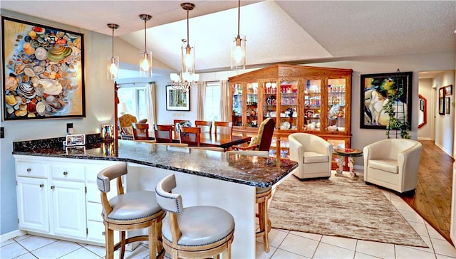 811 E Township St, Fayetteville, AR 72703 - kitchen featuring lofted ceiling, a peninsula, light tile patterned flooring, dark stone counters, and a chandelier