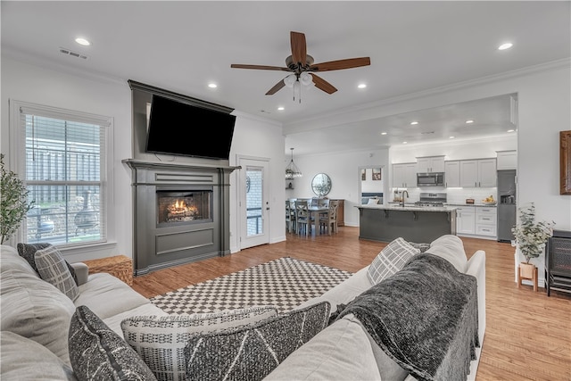 1461 Colonel Mcneil Dr, Prairie Grove, AR 72753 - living room with a ceiling fan, crown molding, light wood finished floors, a glass covered fireplace, and recessed lighting