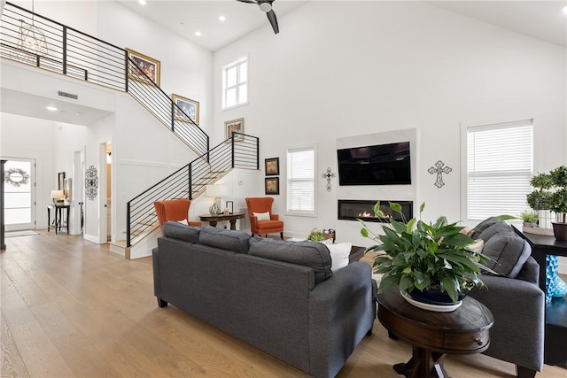 301 SW Autumn Hills Rd, Bentonville, AR 72712 - living area with a high ceiling, light wood-style flooring, stairs, a ceiling fan, and a glass covered fireplace