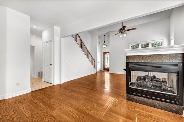 4801 SW Golden Eagle Ave, Bentonville, AR 72713 - unfurnished living room featuring ceiling fan, a multi sided fireplace, wood finished floors, stairway, and a high ceiling