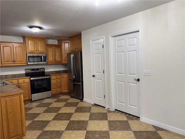 12305 Tyson Rd, Lowell, AR 72745 - kitchen with stainless steel appliances, dark countertops, a textured ceiling, and brown cabinets