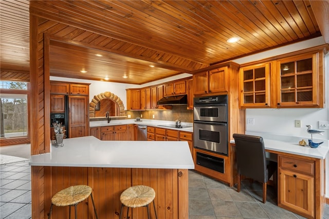 8093 Rockwood Ln, Rogers, AR 72756 - kitchen with stainless steel appliances, a sink, under cabinet range hood, brown cabinetry, and wooden ceiling