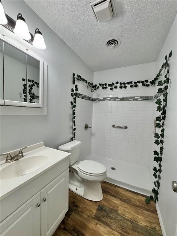 29 5th Ave, Dardanelle, AR 72834 - bathroom with wood finished floors, vanity, a textured ceiling, tiled shower, and toilet