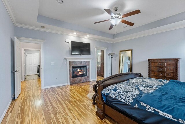 4206 NE Kenton Ave, Bentonville, AR 72712 - bedroom featuring light wood-style flooring, a tray ceiling, a tile fireplace, baseboards, and crown molding