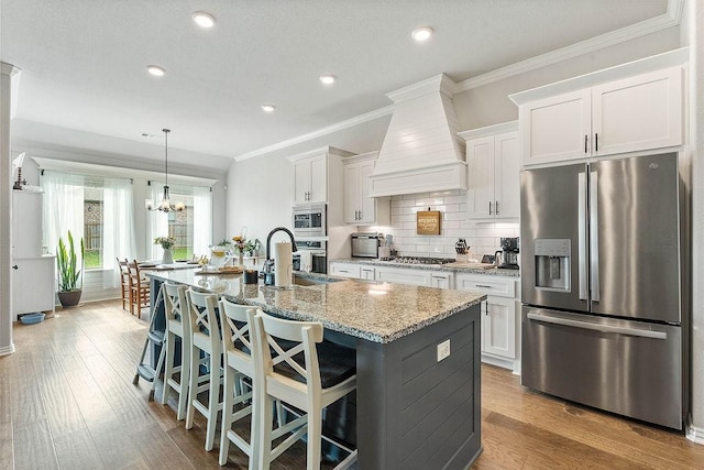 1904 Bergman Rd, Pea Ridge, AR 72751 - kitchen with stainless steel appliances, a kitchen island with sink, white cabinetry, wall chimney exhaust hood, and light stone counters