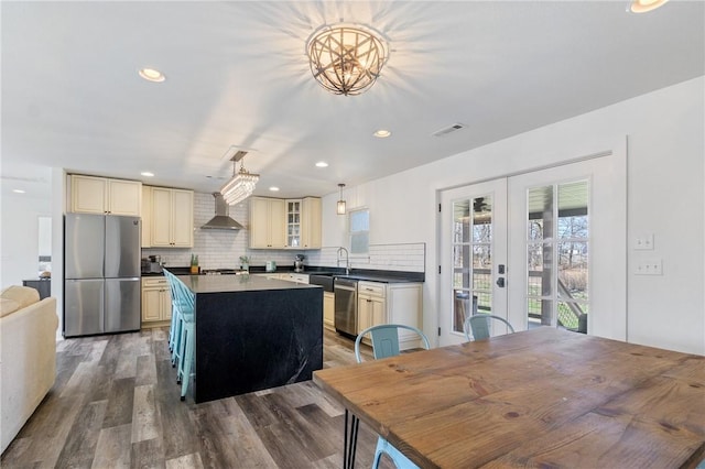 12698 Bush Rd, Centerton, AR 72719 - kitchen featuring appliances with stainless steel finishes, cream cabinets, french doors, dark countertops, and wall chimney exhaust hood