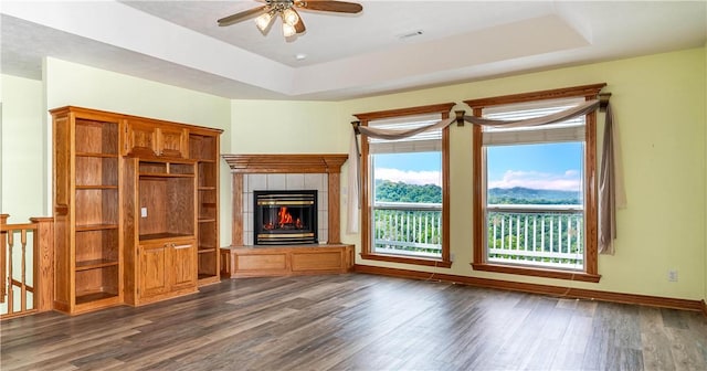 17 La Costa Dr, Holiday Island, AR 72631 - unfurnished living room with dark wood-type flooring, ceiling fan, a raised ceiling, a tiled fireplace, and baseboards