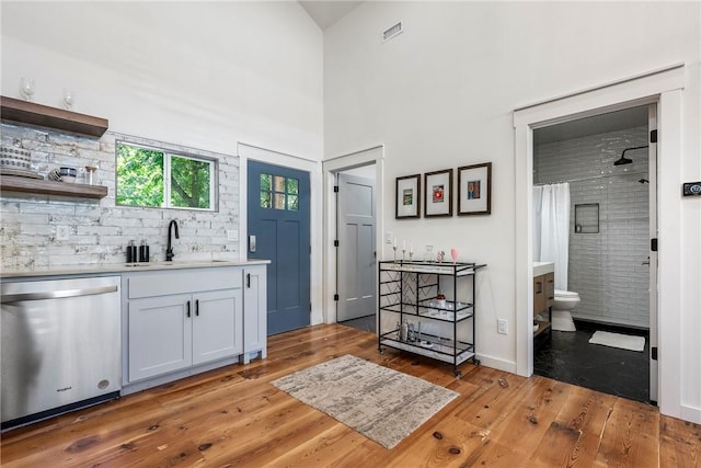 327 S E Ave, Fayetteville, AR 72701 - kitchen with stainless steel dishwasher, light wood-type flooring, light countertops, a high ceiling, and decorative backsplash
