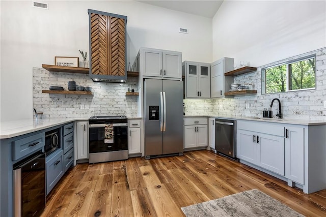 327 S E Ave, Fayetteville, AR 72701 - kitchen featuring appliances with stainless steel finishes, open shelves, backsplash, a towering ceiling, and wood finished floors