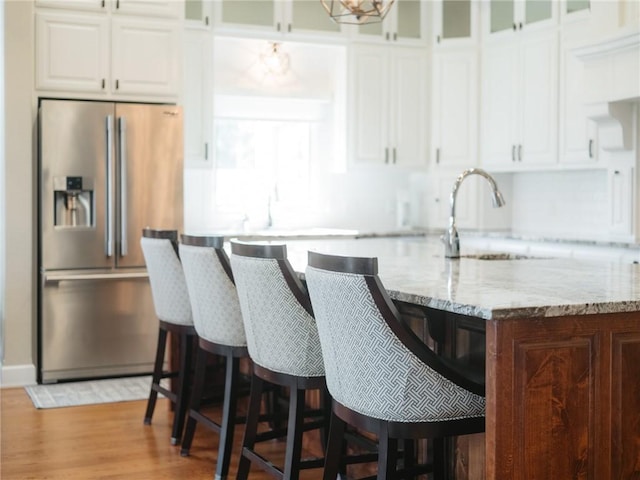 42 Devizis Dr, Bella Vista, AR 72714 - kitchen with stainless steel fridge, a sink, light stone counters, white cabinetry, and glass insert cabinets