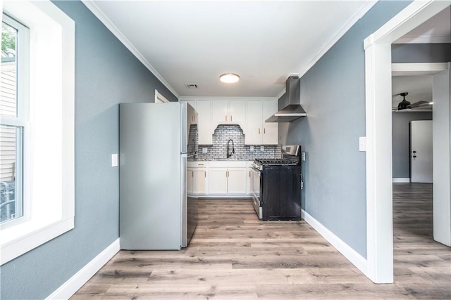 2532 E 4th St, Tulsa, OK 74104 - kitchen featuring stainless steel range with gas cooktop, freestanding refrigerator, wall chimney exhaust hood, crown molding, and white cabinets