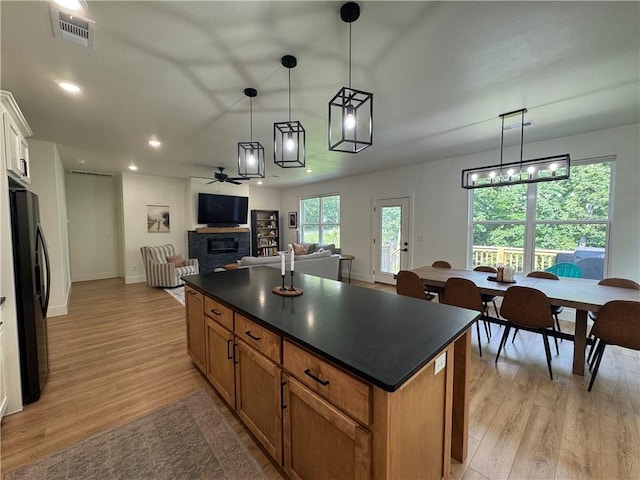 1 Llanon Cir, Bella Vista, AR 72714 - kitchen with black refrigerator with ice dispenser, dark countertops, ceiling fan, a stone fireplace, and light wood-style floors