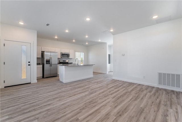 1071 Kentucky Ave, Bentonville, AR 72713 - kitchen featuring appliances with stainless steel finishes, open floor plan, light wood finished floors, white cabinets, and an island with sink