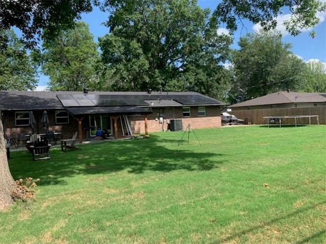 712 Carlton St, Springdale, AR 72762 - back of house with a trampoline, central AC, roof mounted solar panels, a patio area, and a fire pit