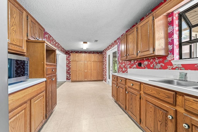 634 Orchard View Ests, Alma, AR 72921 - kitchen featuring wallpapered walls, stainless steel microwave, a textured ceiling, light countertops, and brown cabinets