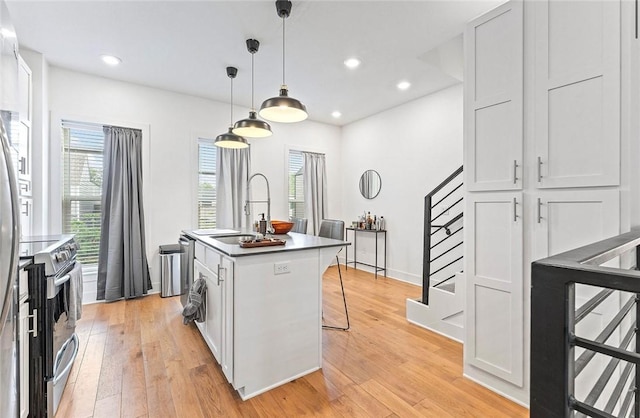 429 SW B St, Bentonville, AR 72712 - kitchen featuring stainless steel electric stove, a sink, light wood-type flooring, a center island with sink, and a breakfast bar