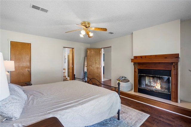 13004 Canehill Rd, Lincoln, AR 72744 - bedroom with wood finished floors, a glass covered fireplace, a textured ceiling, and ceiling fan