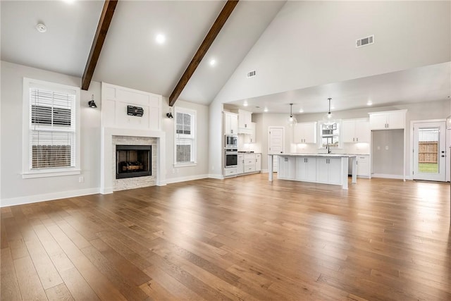 1221 Red Maple St, Centerton, AR 72719 - unfurnished living room featuring high vaulted ceiling, light wood finished floors, beamed ceiling, a sink, and a fireplace