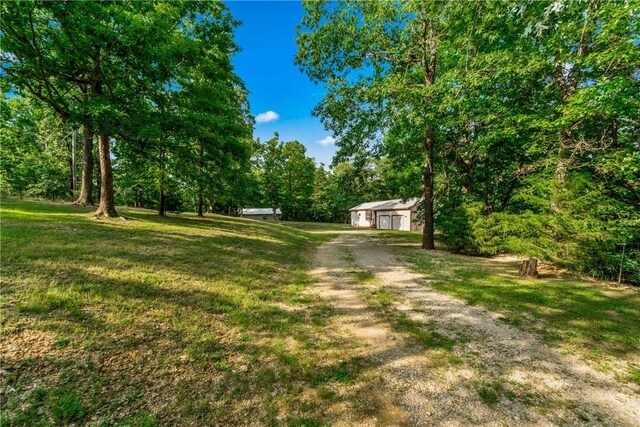11648 Ventris Rd, Garfield, AR 72732 - view of green lawn with an outdoor structure, a detached garage, dirt driveway, and a forest view