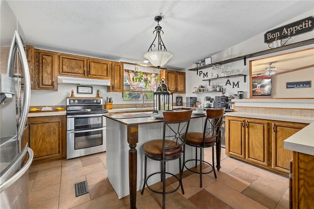18246 Oakridge Rd, Springdale, AR 72764 - kitchen with appliances with stainless steel finishes, brown cabinetry, a kitchen island, under cabinet range hood, and a textured ceiling