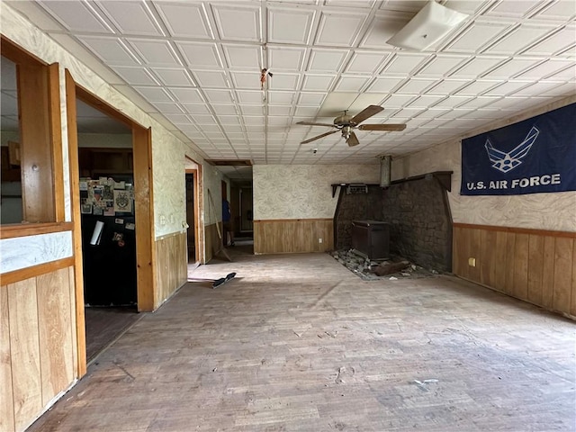 13888 White Oak Ln, Bentonville, AR 72712 - unfurnished living room featuring a wood stove, a wainscoted wall, wood walls, wood finished floors, and a ceiling fan
