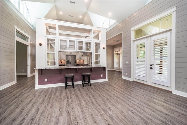 19643 Indigo Dr, Rogers, AR 72756 - kitchen featuring stainless steel refrigerator with ice dispenser, wooden walls, a kitchen bar, baseboards, and wood finished floors