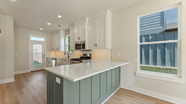 1209 SW Journey Ln, Bentonville, AR 72713 - kitchen with stainless steel appliances, decorative backsplash, light wood-style flooring, light countertops, and white cabinets