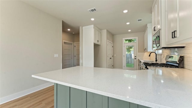 1209 SW Journey Ln, Bentonville, AR 72713 - kitchen with stainless steel appliances, a peninsula, light stone countertops, tasteful backsplash, and light wood-style flooring